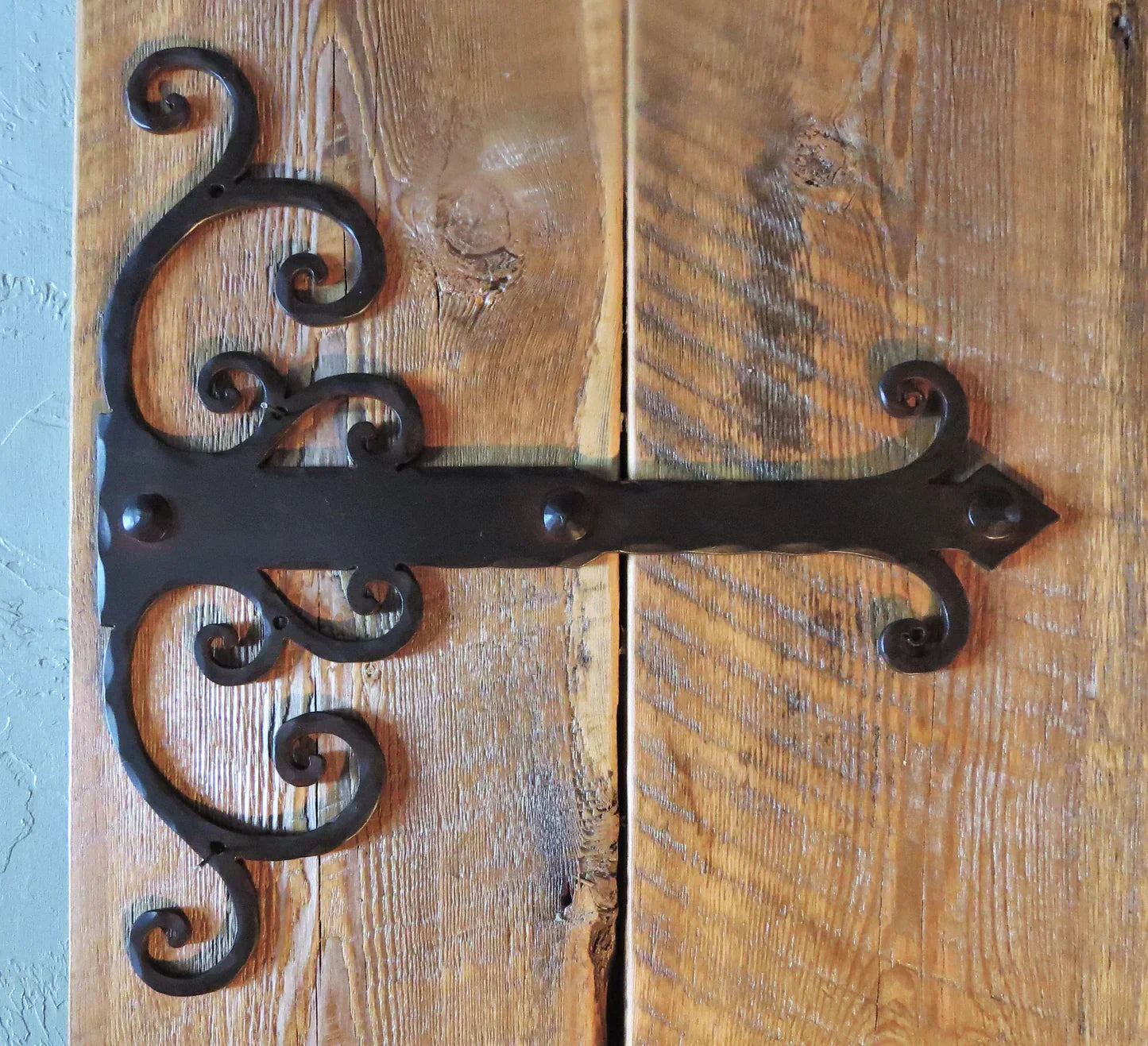 Decorative black hinge strap with scroll design on rustic wooden door background