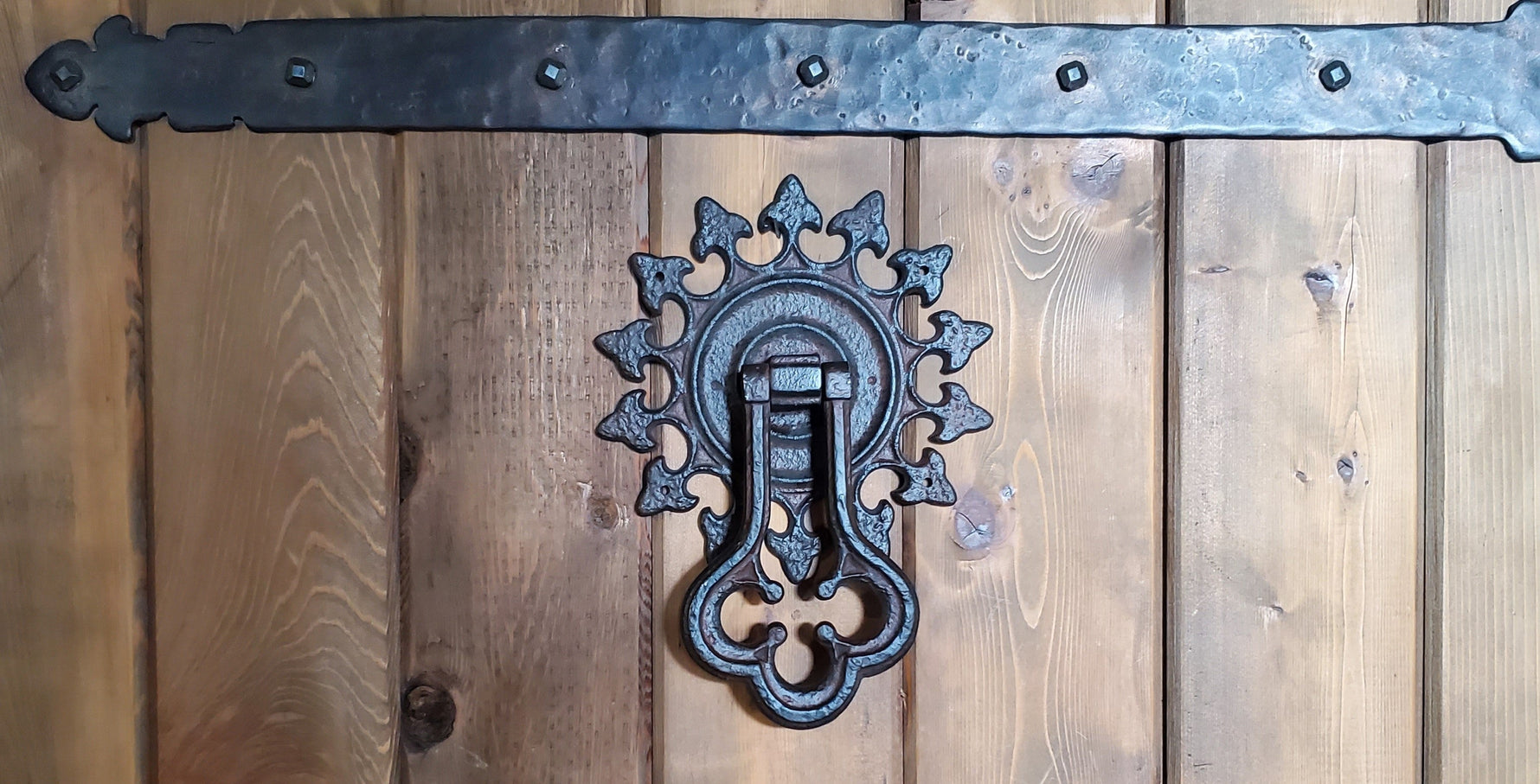 Ornate Portuguese Gothic iron door knocker on a wooden door with a decorative strap