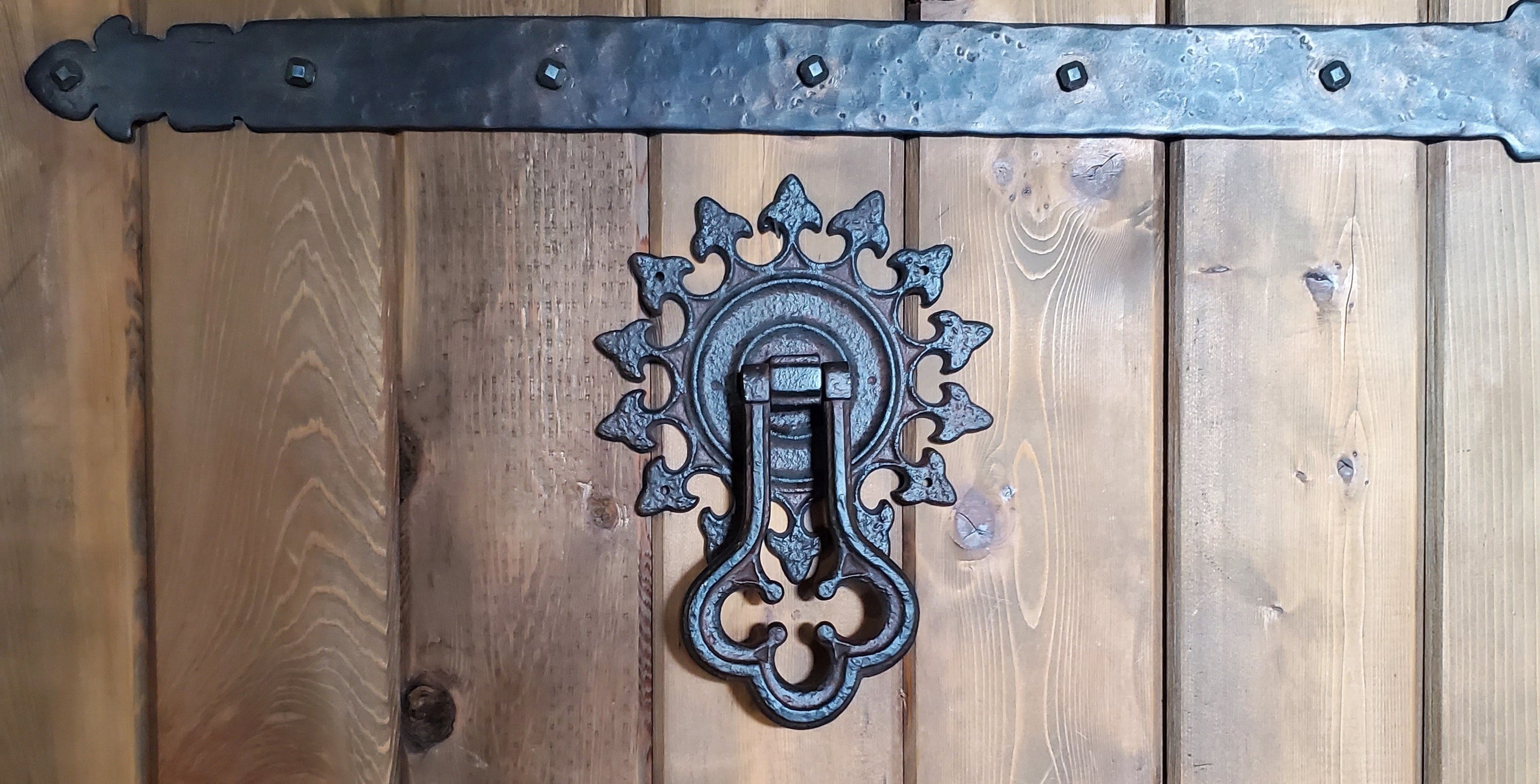 Ornate Portuguese Gothic iron door knocker on a wooden door with a decorative strap