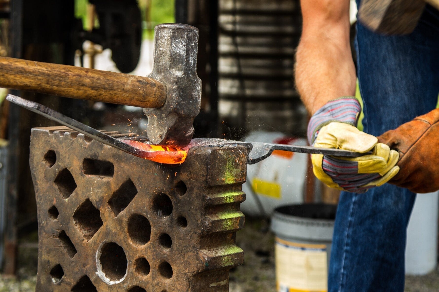 Blacksmith hammer striking hot metal on an anvil with sparks flying in a workshop