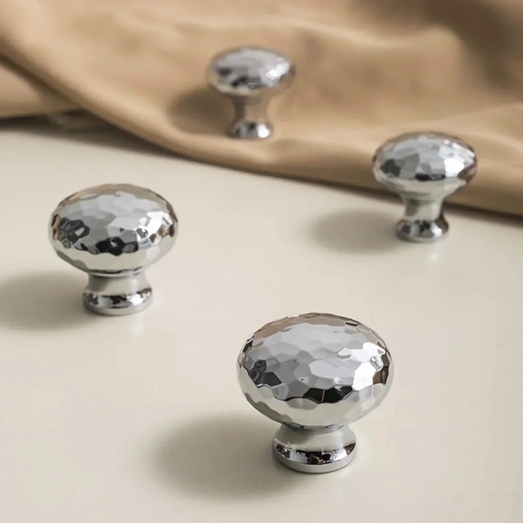 polished chrome cabinet knobs with a hammered texture on a neutral background