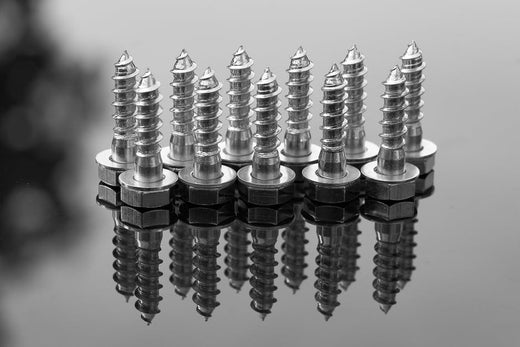 Collection of polished lag bolts with nuts reflecting on a dark surface