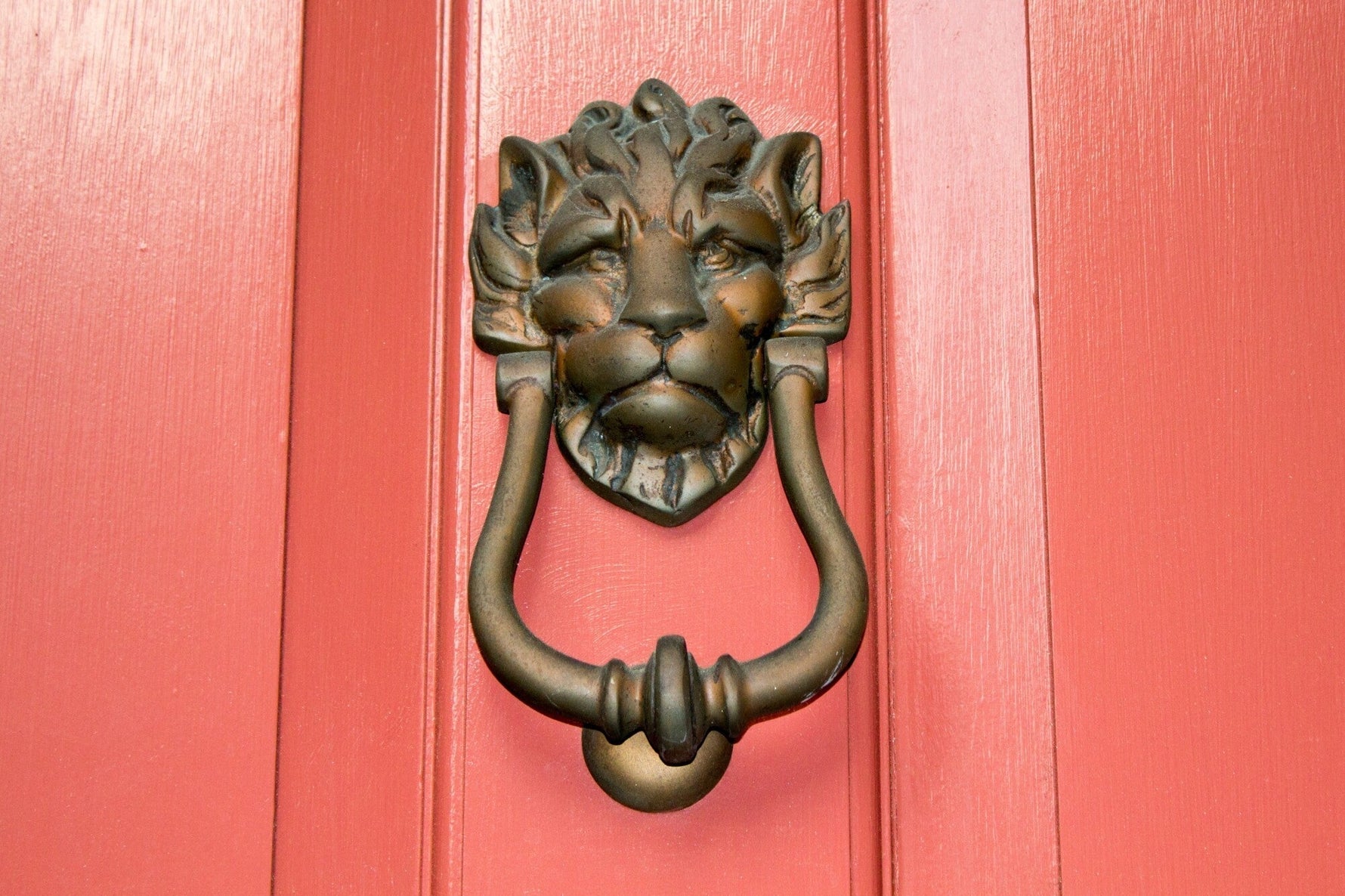 Lion head door knocker on a red door, showcasing elegant home exterior decor