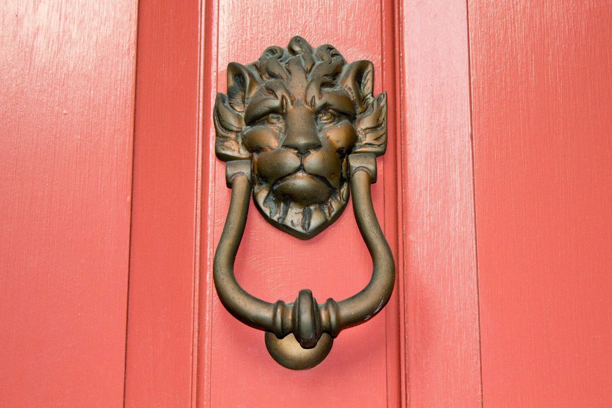 Lion head door knocker on a red door, showcasing elegant home exterior decor