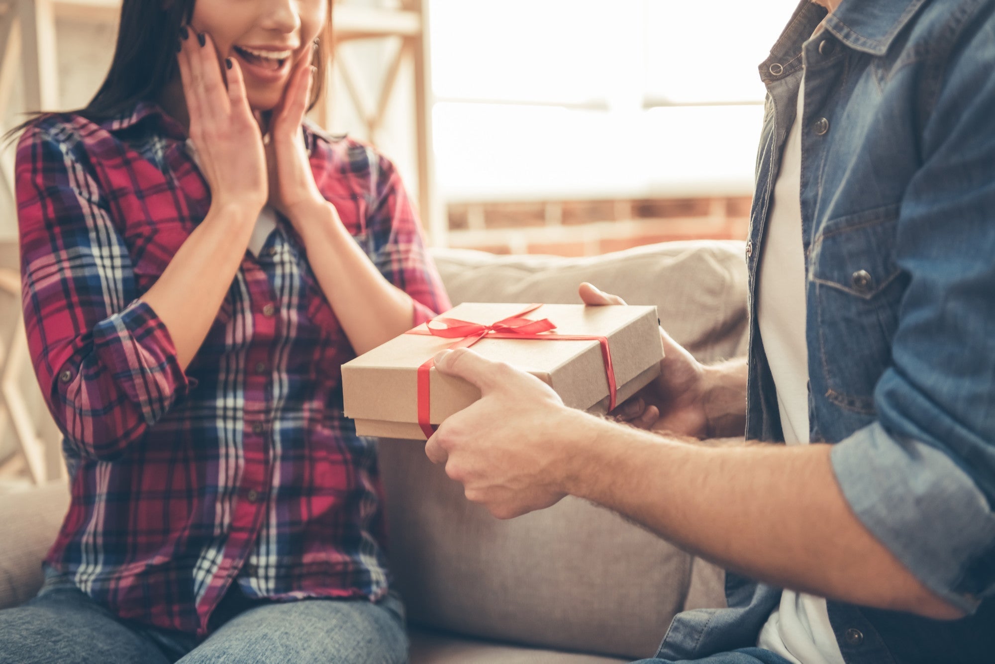 excited woman receiving a surprise gift from her partner on anniversary celebration