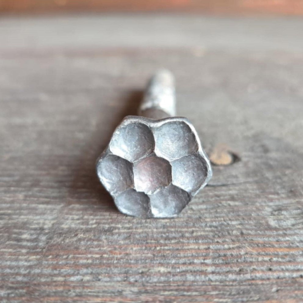 A silver-colored metal bolt with a flower head design, placed on a wooden surface.