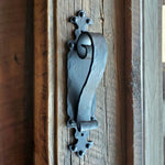 Black iron door pull handle with gothic cathedral inspired design, positioned on a wooden surface.