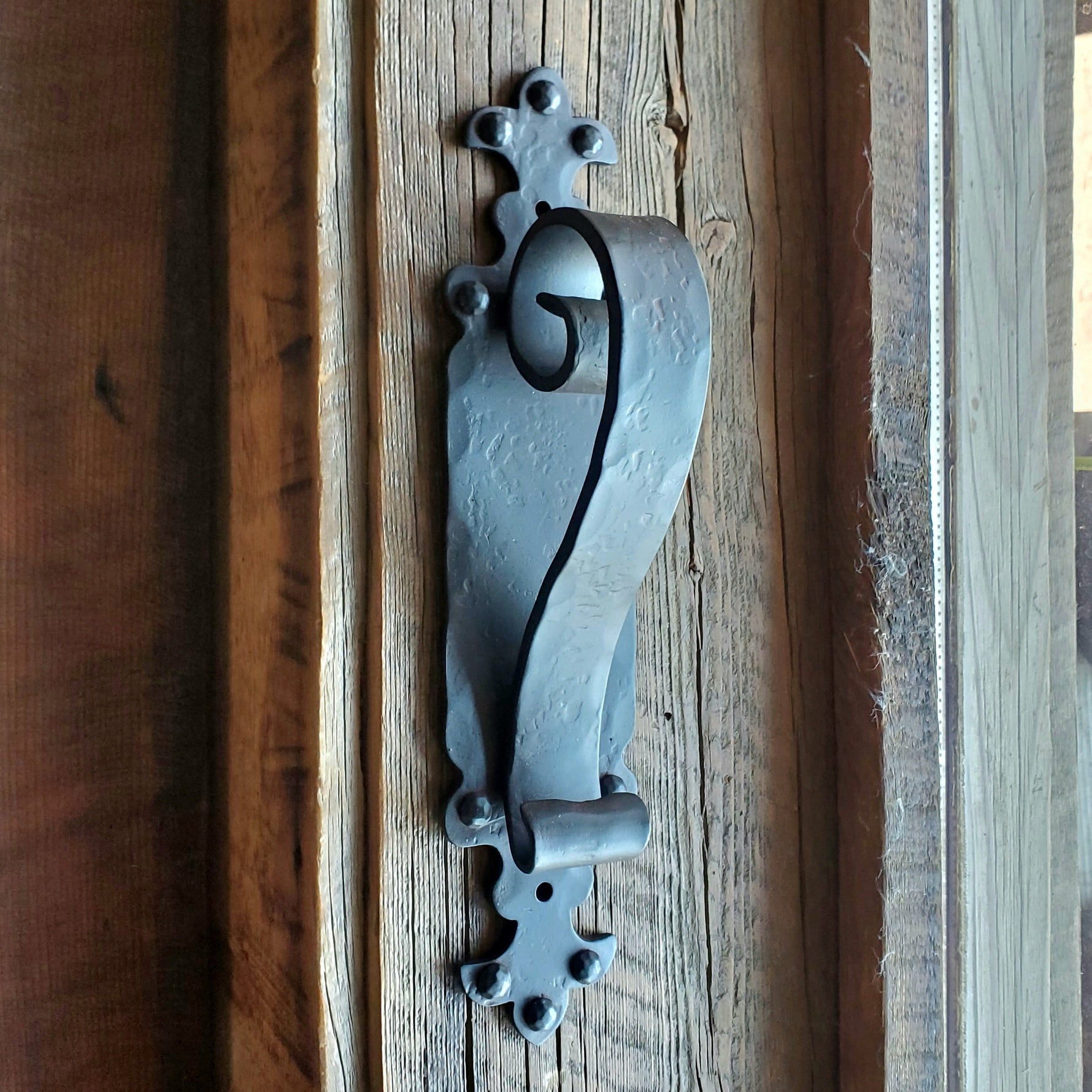 Black iron door pull handle with gothic cathedral inspired design, positioned on a wooden surface.