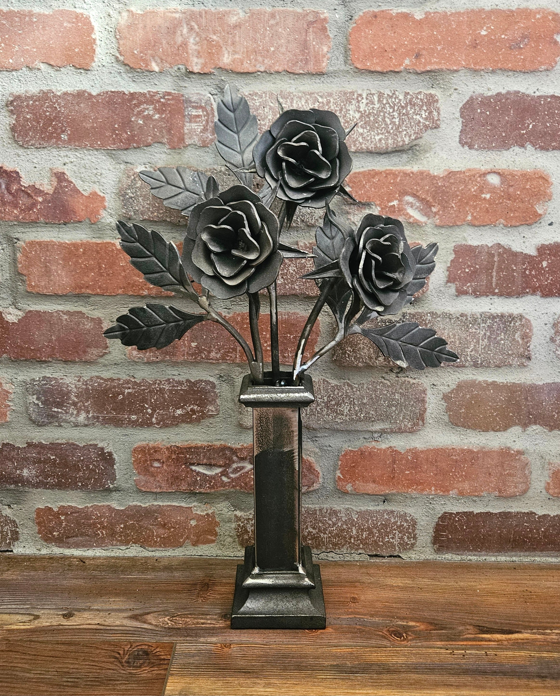Decorative metal flower sculpture on a stand against a brick wall.