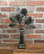 Decorative metal flower sculpture on a stand against a brick wall.
