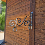 Decorative metal hook on a wooden wall with blurred greenery in the background