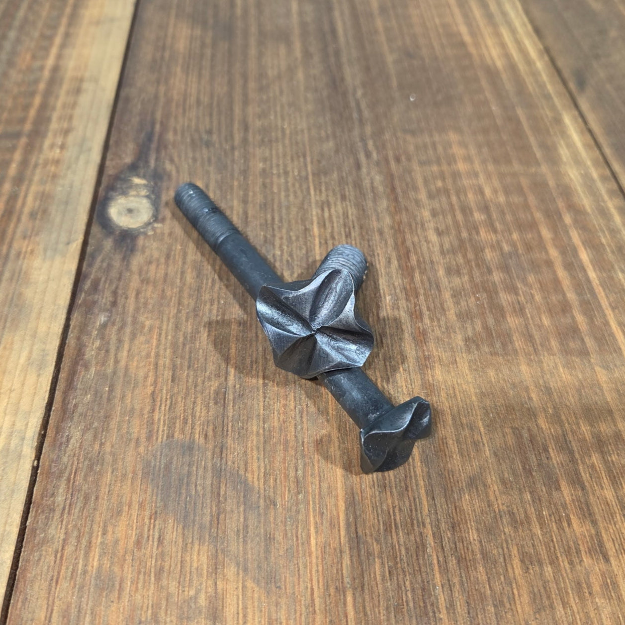 A hand hammered cross square head bolt with a wrought iron finish on a wood background.