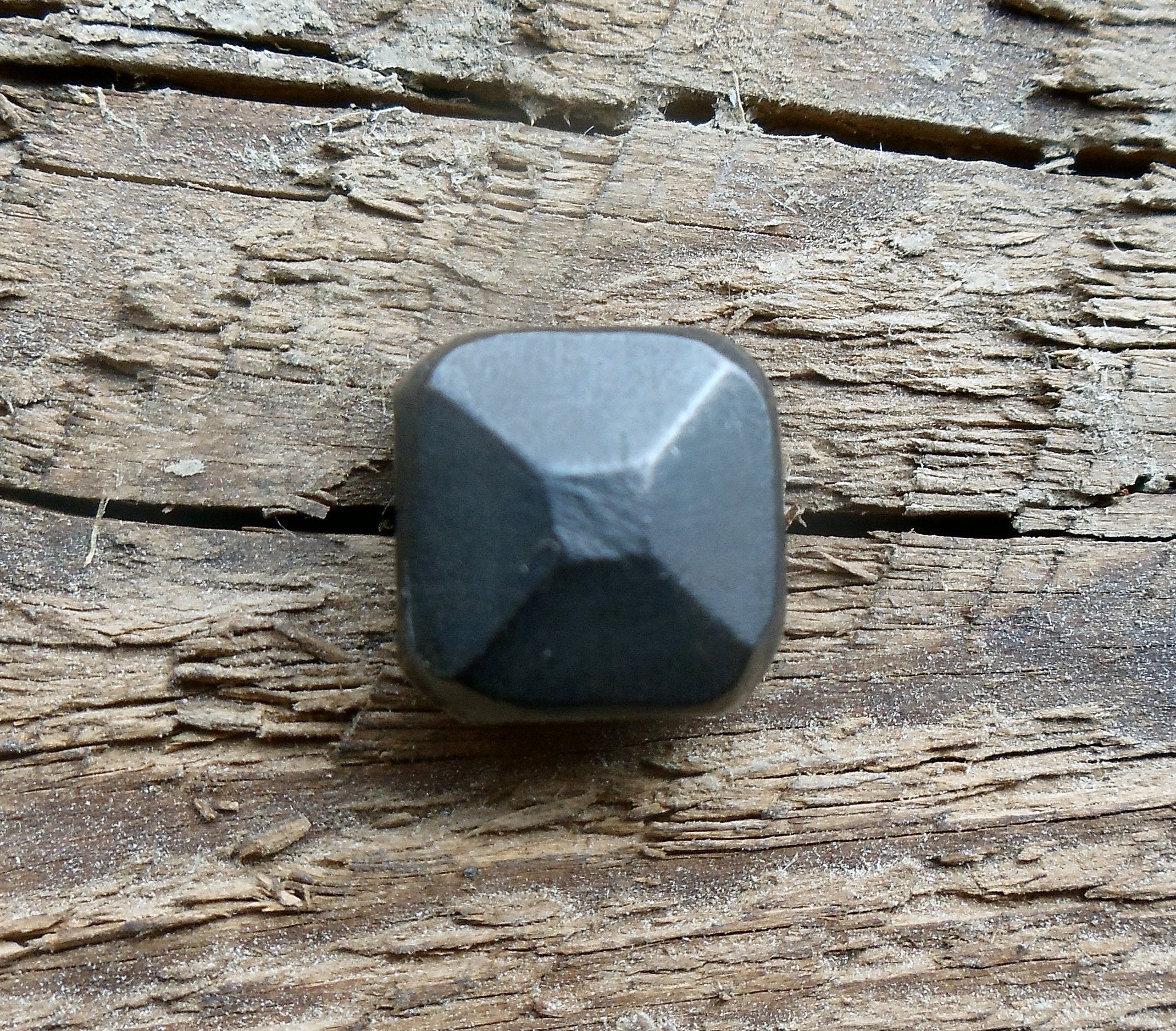 A thick square pyramid head decorative screw displayed on a wooden surface.