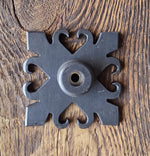 A black 15th century iron doorstop with a detailed composition, placed on a wooden floor.