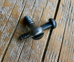 A black antique restoration slotted head screw lying on a wooden surface.