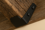 hand forged Black metal bracket with square screw heads on a wooden beam 
