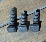 A look at 3 different textured square head bolts distressed, Hammered, and Pyramid all are painted black and finished with a pewter patina on a wood background.