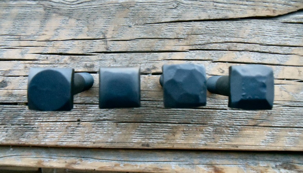 A look of 4 different options for square head bolts smooth, rounded, hammered, pyramid all are painted black on a wood background.  