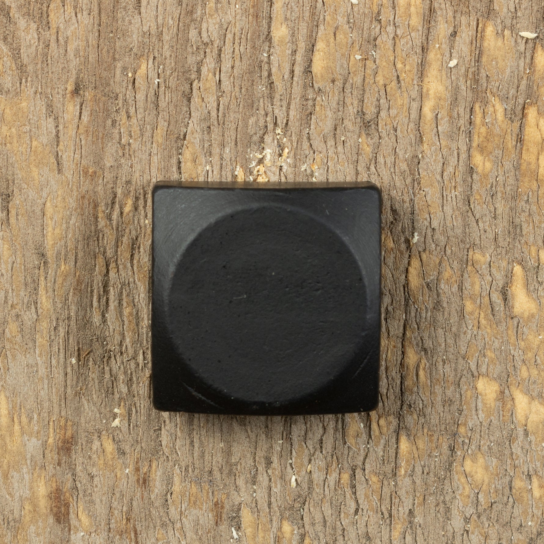A square head bolt with a smooth texture and painted black installed on a wood background.
