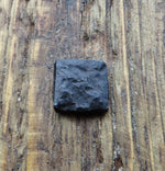 A top view of a square head lag that has been distressed and painted black installed in a wood background