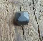 A thick square pyramid head decorative screw displayed on a wooden surface.