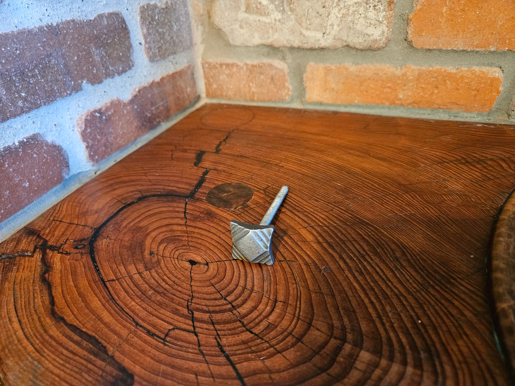 A side view of an ornate tapered square head bolt with a raw finish on a wood background.