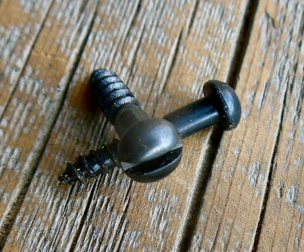 A black antique restoration slotted head bubble screw lying on a wooden surface.