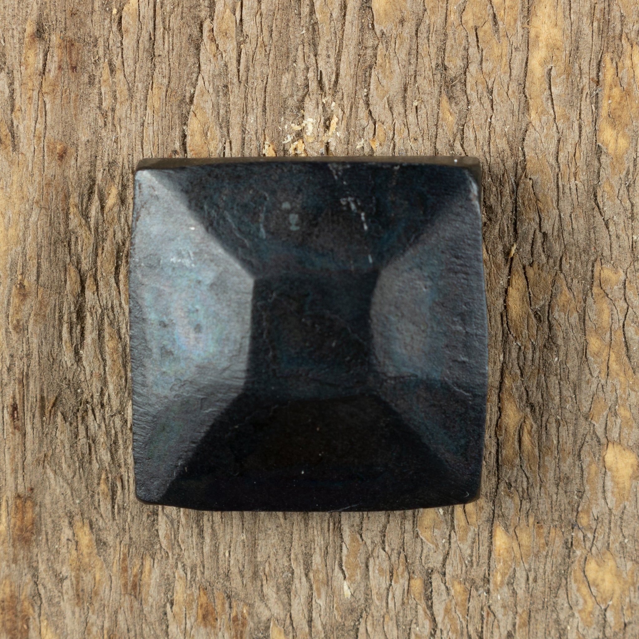 A top view of a hand hammered pyramid square head lag that has a gun metal finish that is installed on a wood background