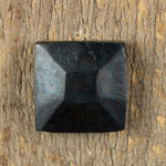 A top view of a hand hammered pyramid square head lag that has a gun metal finish that is installed on a wood background