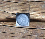 A square head bolt that has a smooth texture and is painted black and finished with aged pewter patina installed on a wood background. 