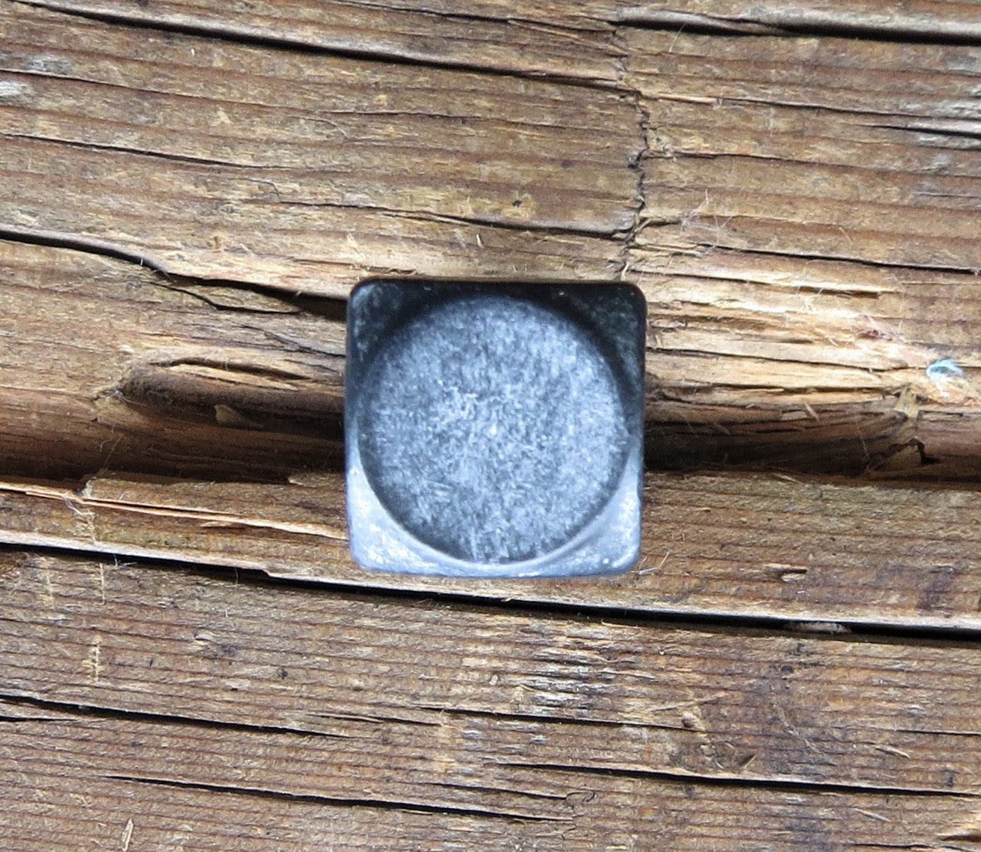 A square head bolt that has a smooth texture and is painted black and finished with aged pewter patina installed on a wood background. 