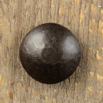 A top view of a carriage bolt that has a smooth texture and is painted black with a aged bronze patina finish.