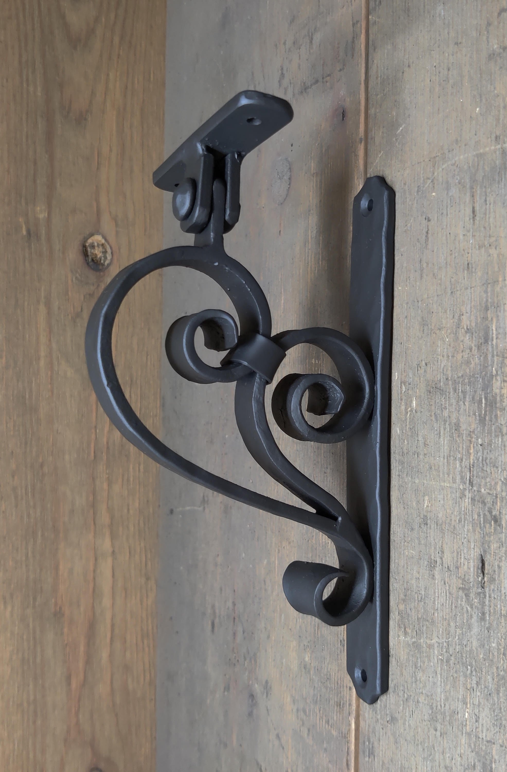A black iron handrail bracket mounted on a wooden surface, featuring a decorative design.