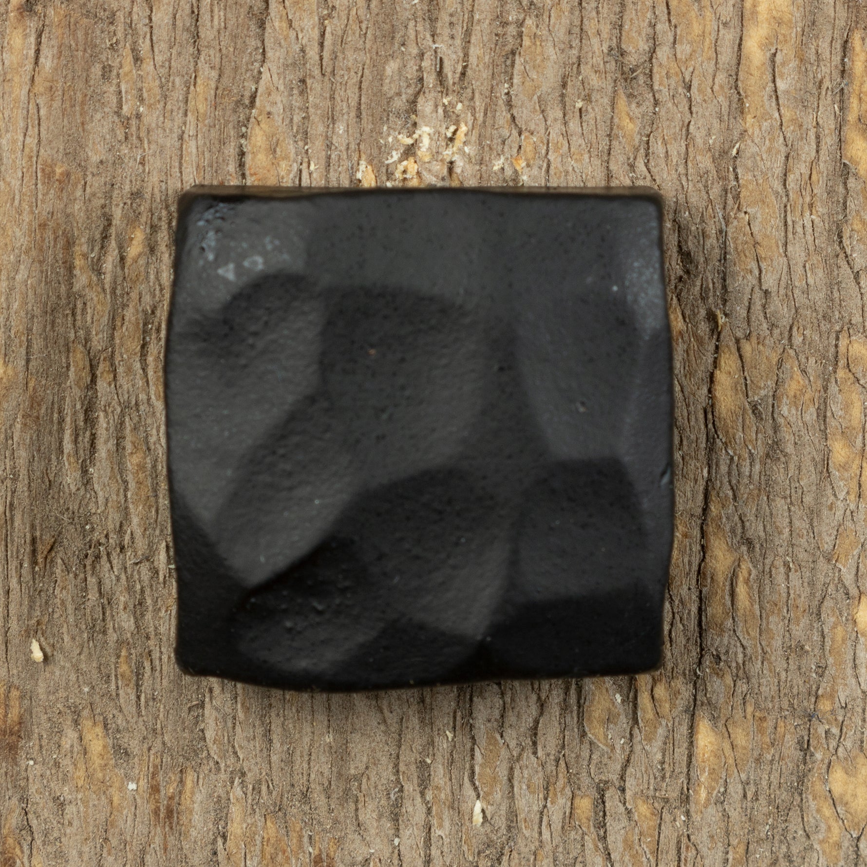 A top view of a hand hammered square head lag that is painted black and screwed into a piece of wood as the background.