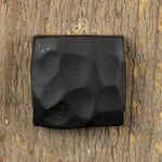 A square head bolt that has been hand hammered and painted black on a wood backround.