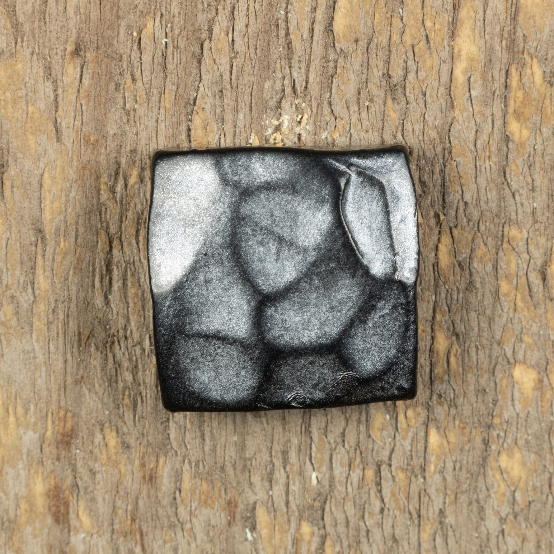 A hand hammered square head bolt that has been painted black and finished with an aged pewter patina.