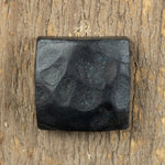A hand hammered square head bolt that has a gun metal finish installed on a wood background.