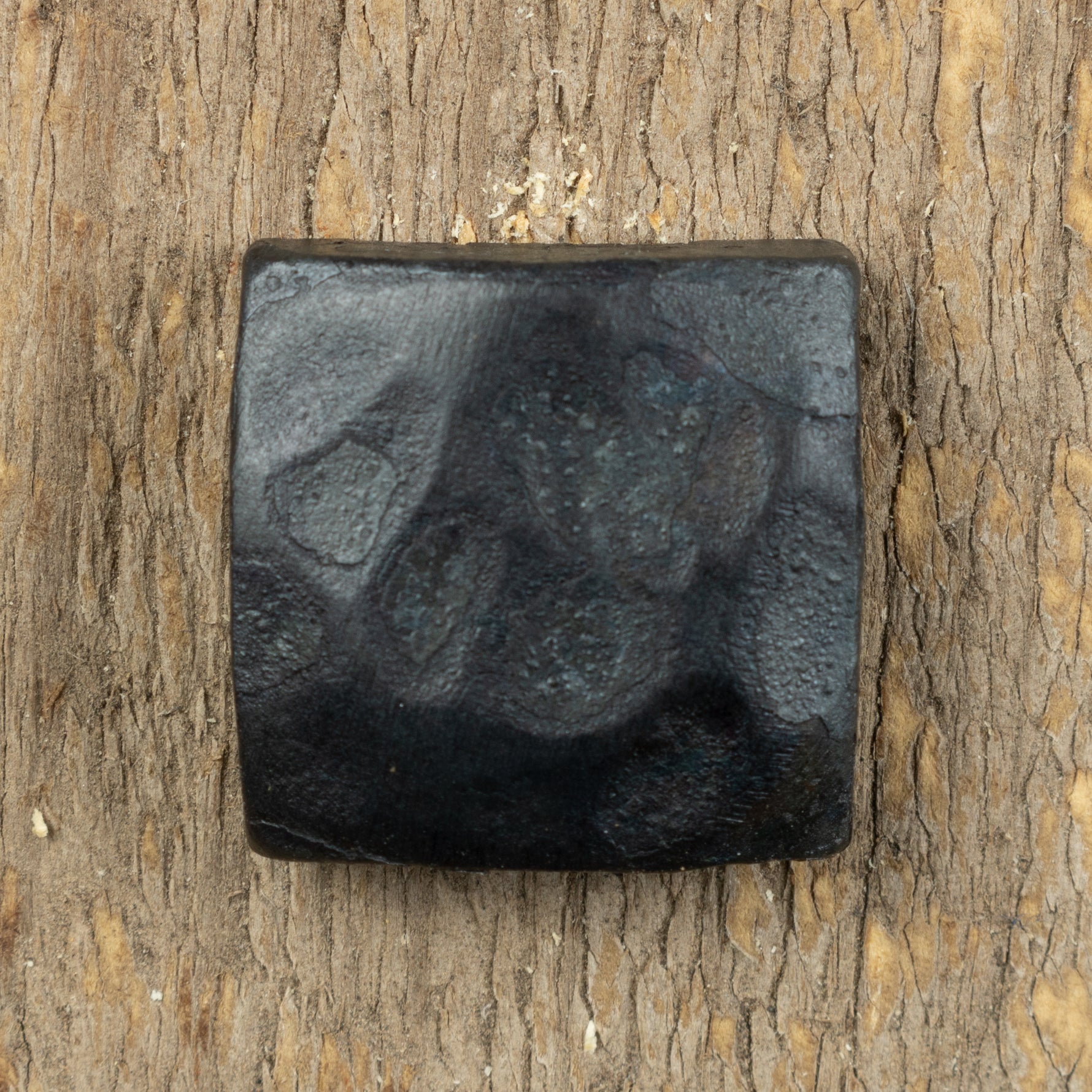 A hand hammered square head bolt that has a gun metal finish installed on a wood background.