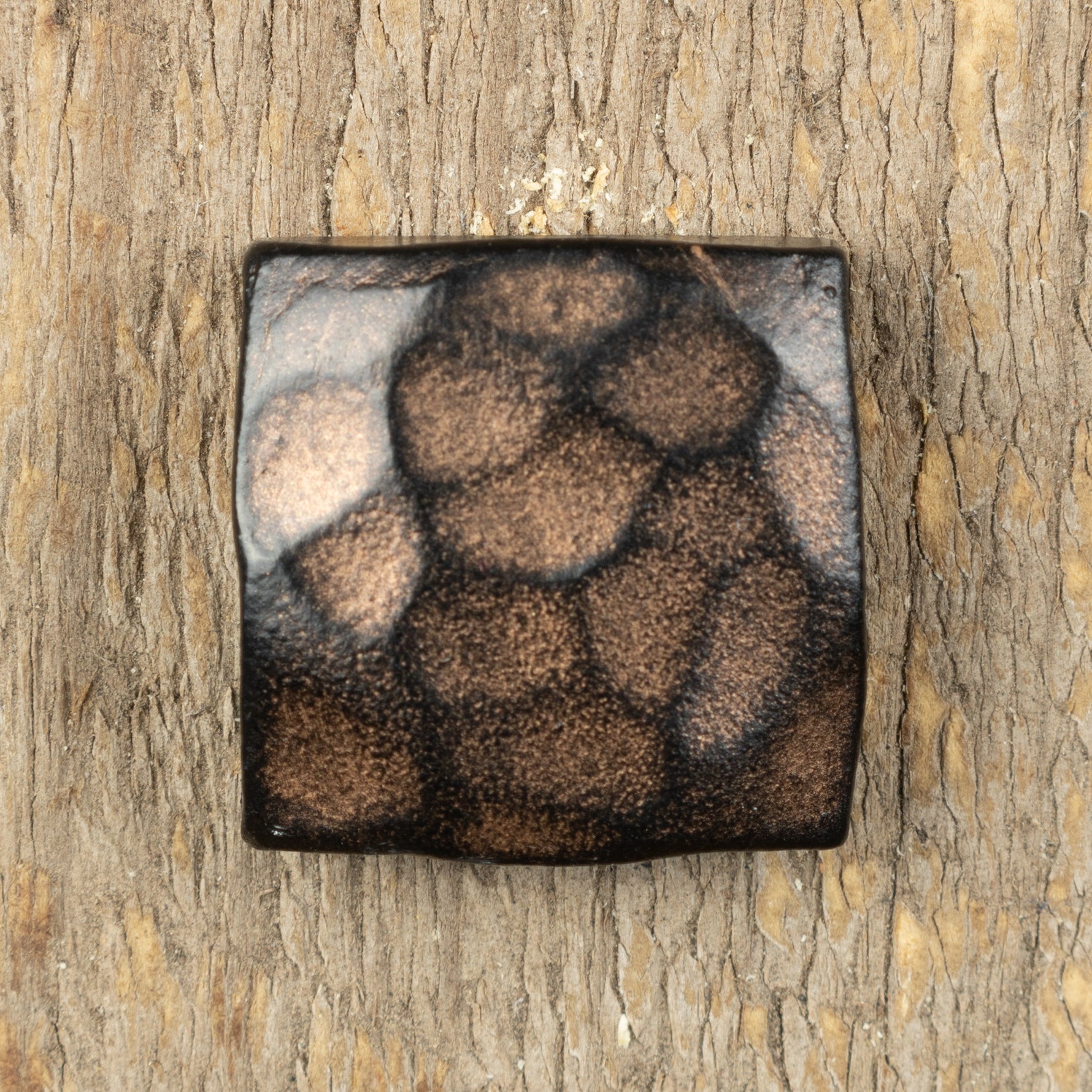 A hand hammered square head bolt that has been painted black and finished with an aged bronze patina.