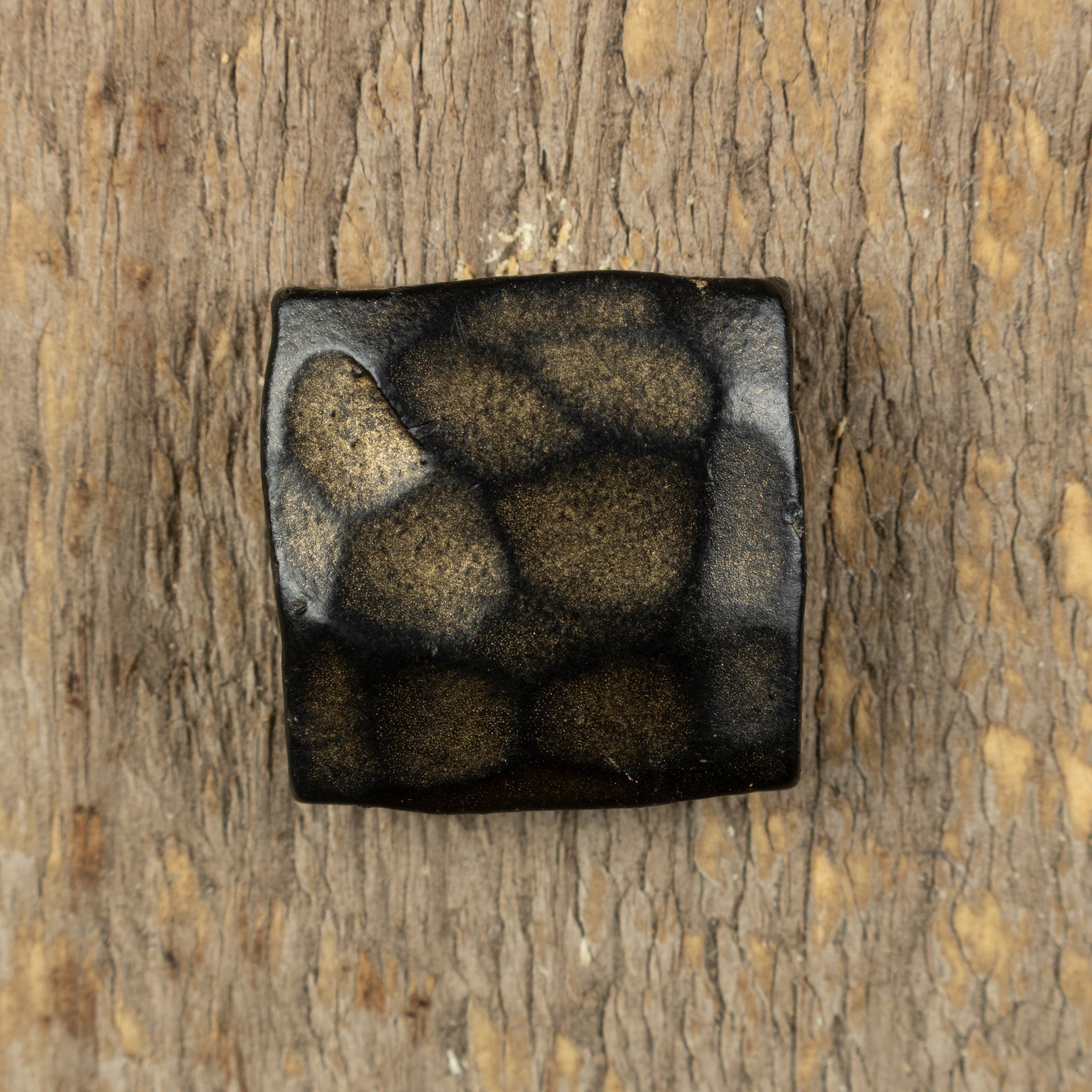 Top view of a hammered square head shows the hand hammered irregular square shape in an aged gold patina finish against a rustic wood background.