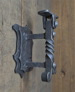 An iron handrail bracket with a decorative design, mounted on a wooden surface.