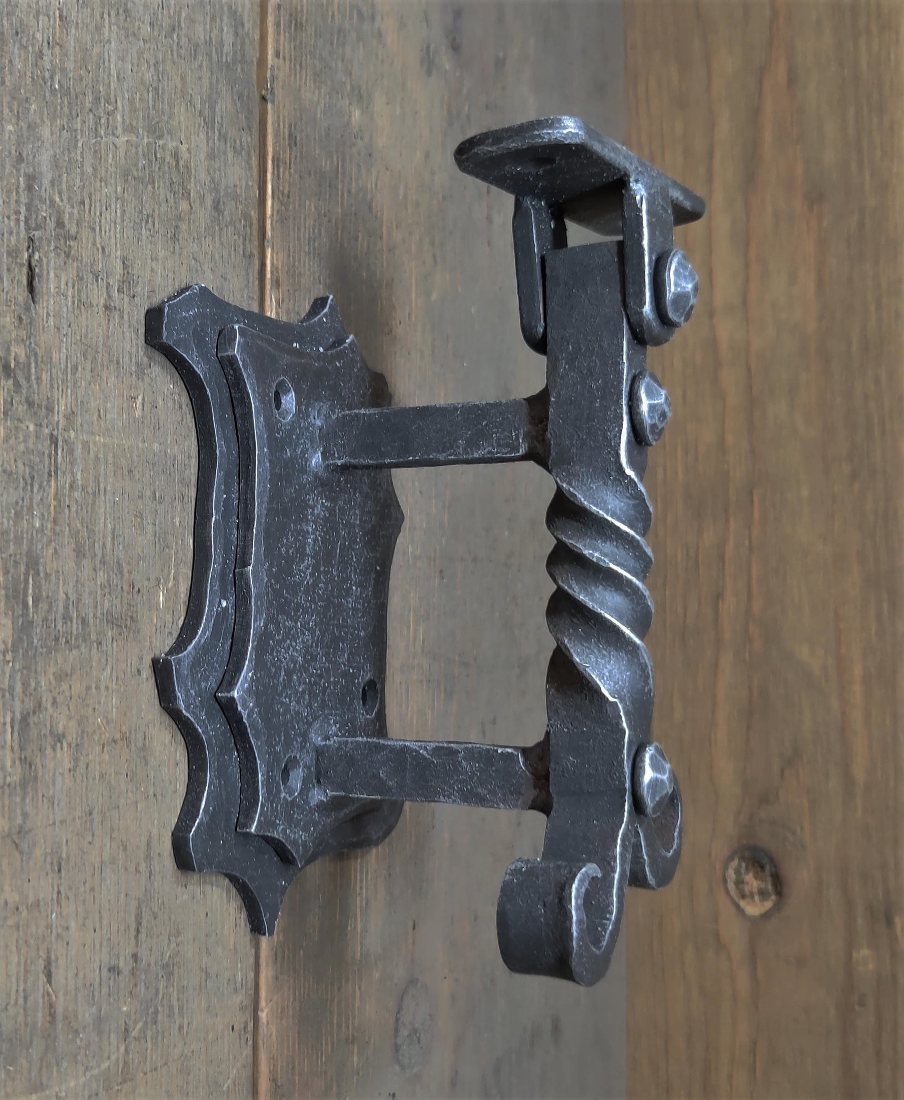 An iron handrail bracket with a decorative design, mounted on a wooden surface.