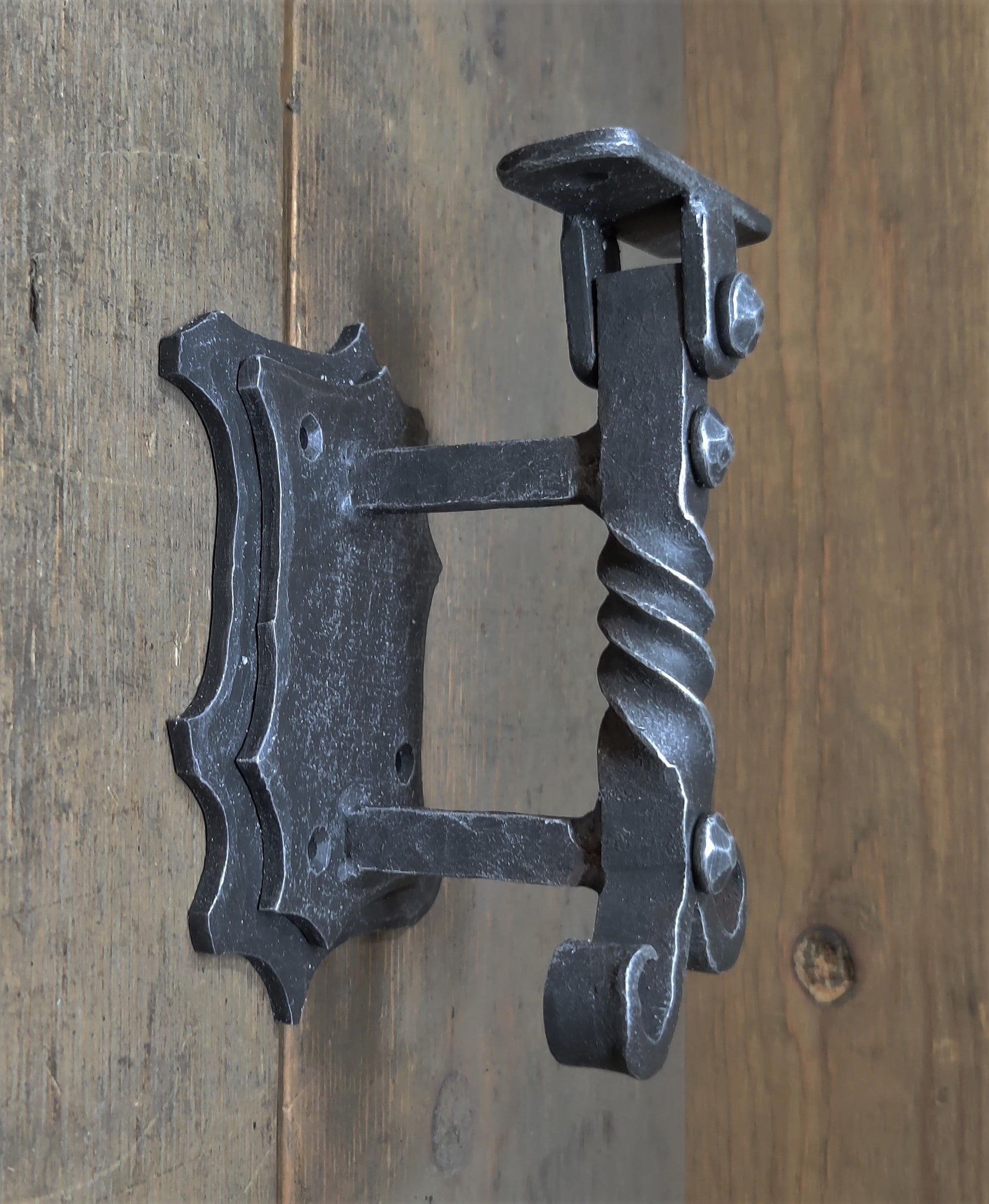 An iron handrail bracket with a decorative design, mounted on a wooden surface.
