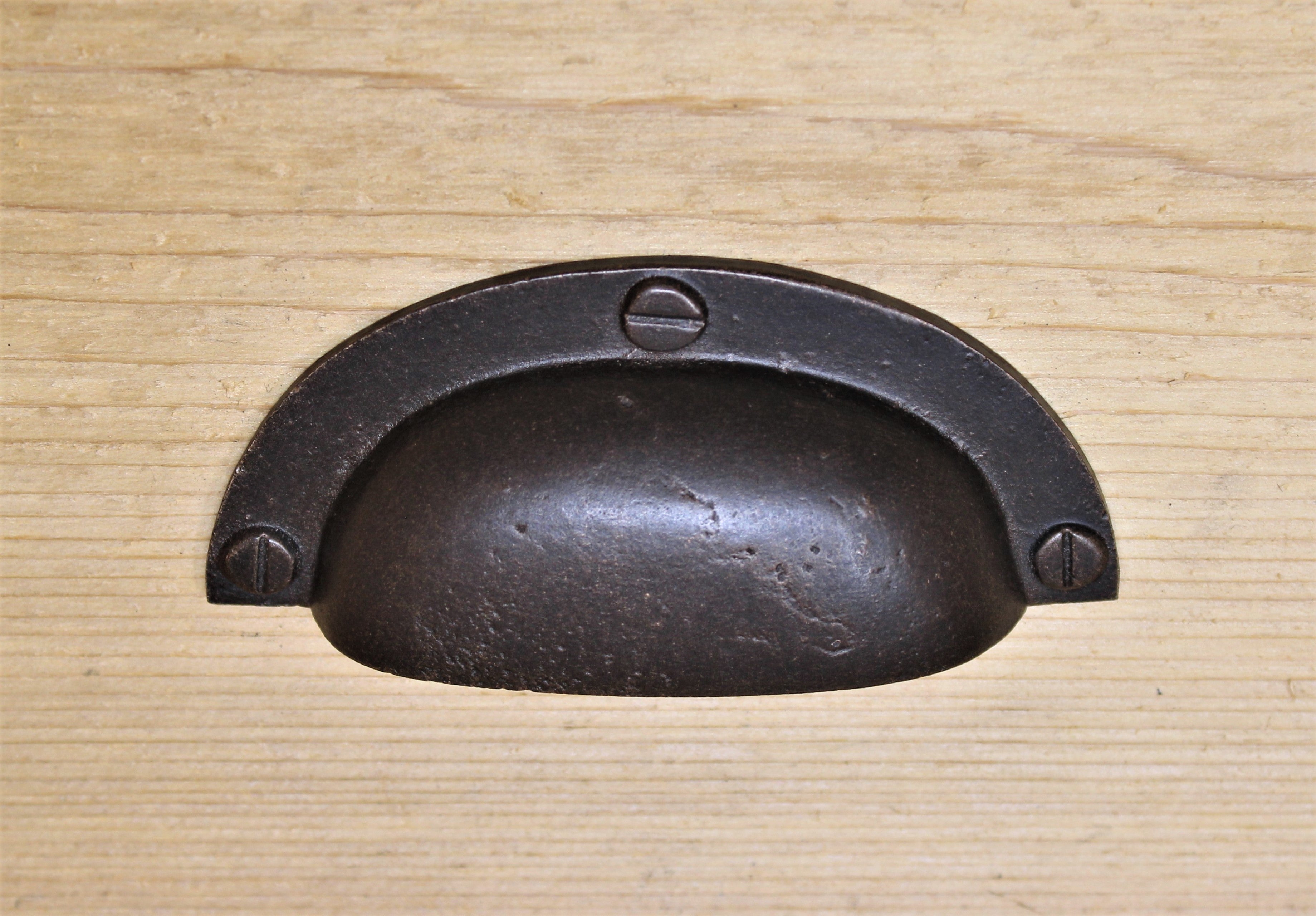 A brown metal farmhouse cup pull drawer knob placed on a wooden surface.