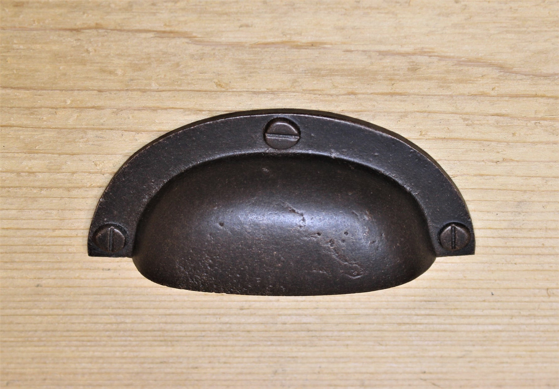 A brown metal farmhouse cup pull drawer knob placed on a wooden surface.