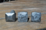 Three examples of hand hammered square head bolts Pyramid Hammered, disstressed, and hammered with a raw finish on a wood background.
