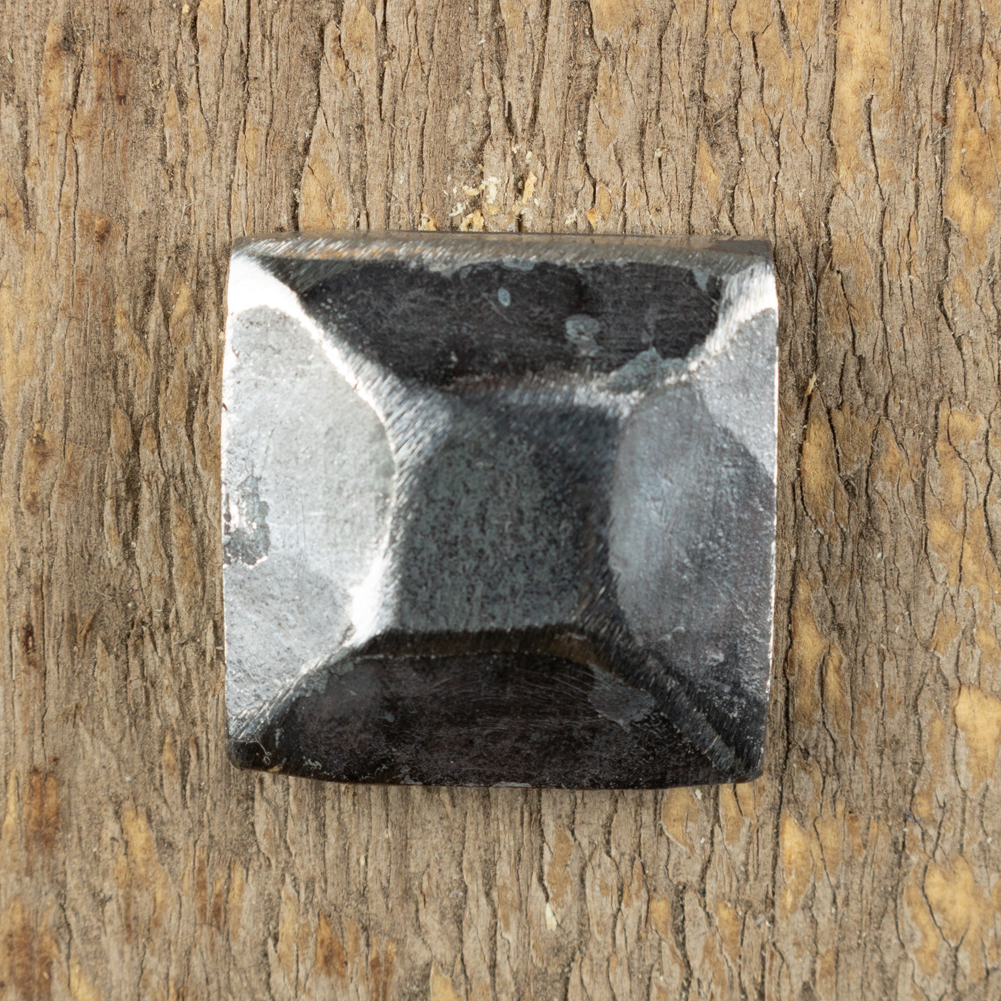 A pyramid hammered square head bolt that is left as raw metal installed on a wood background.