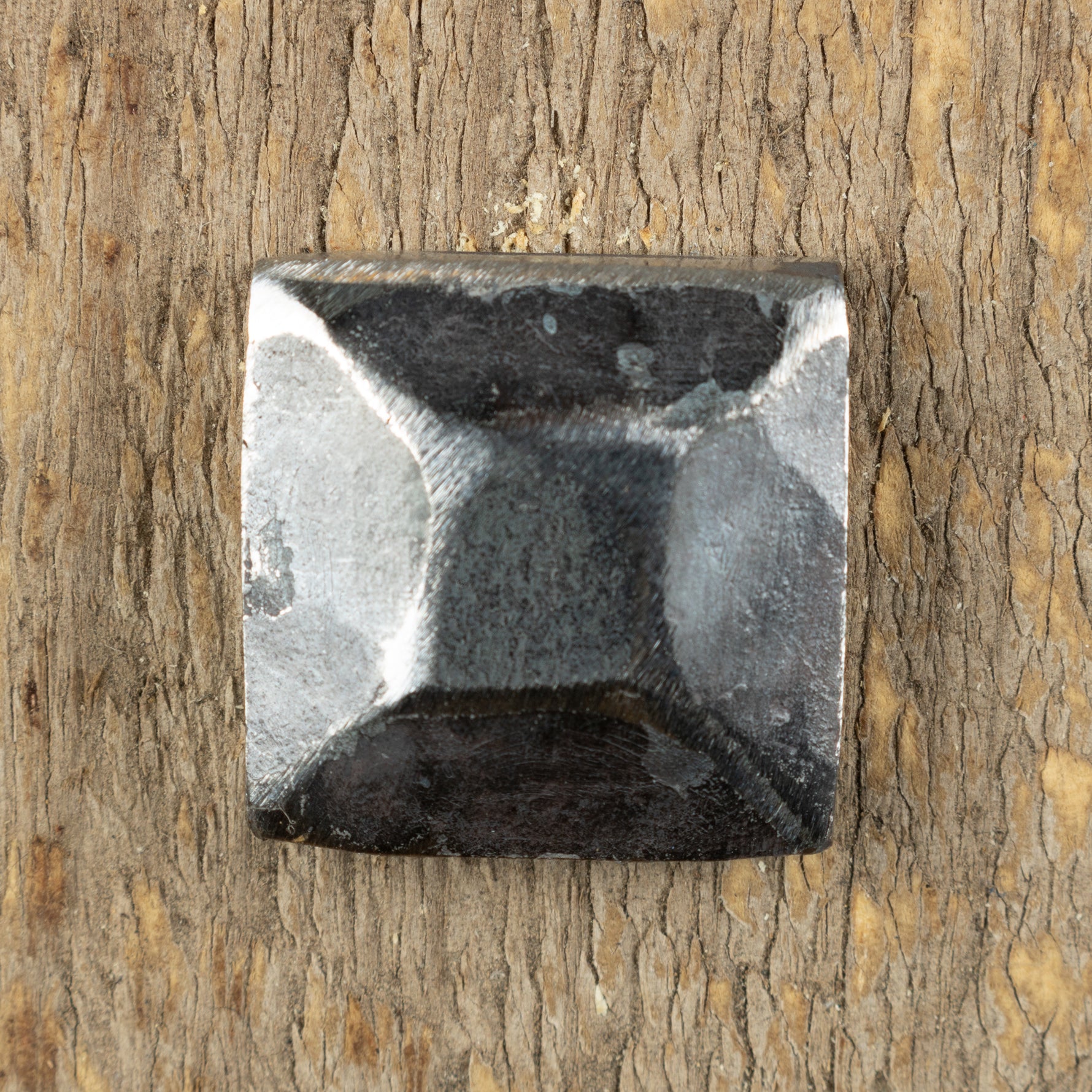 A pyramid hammered square head bolt that is left as raw metal installed on a wood background.
