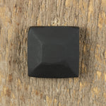 A pyramid hammered square head bolt that has been painted black installed on a wood background.