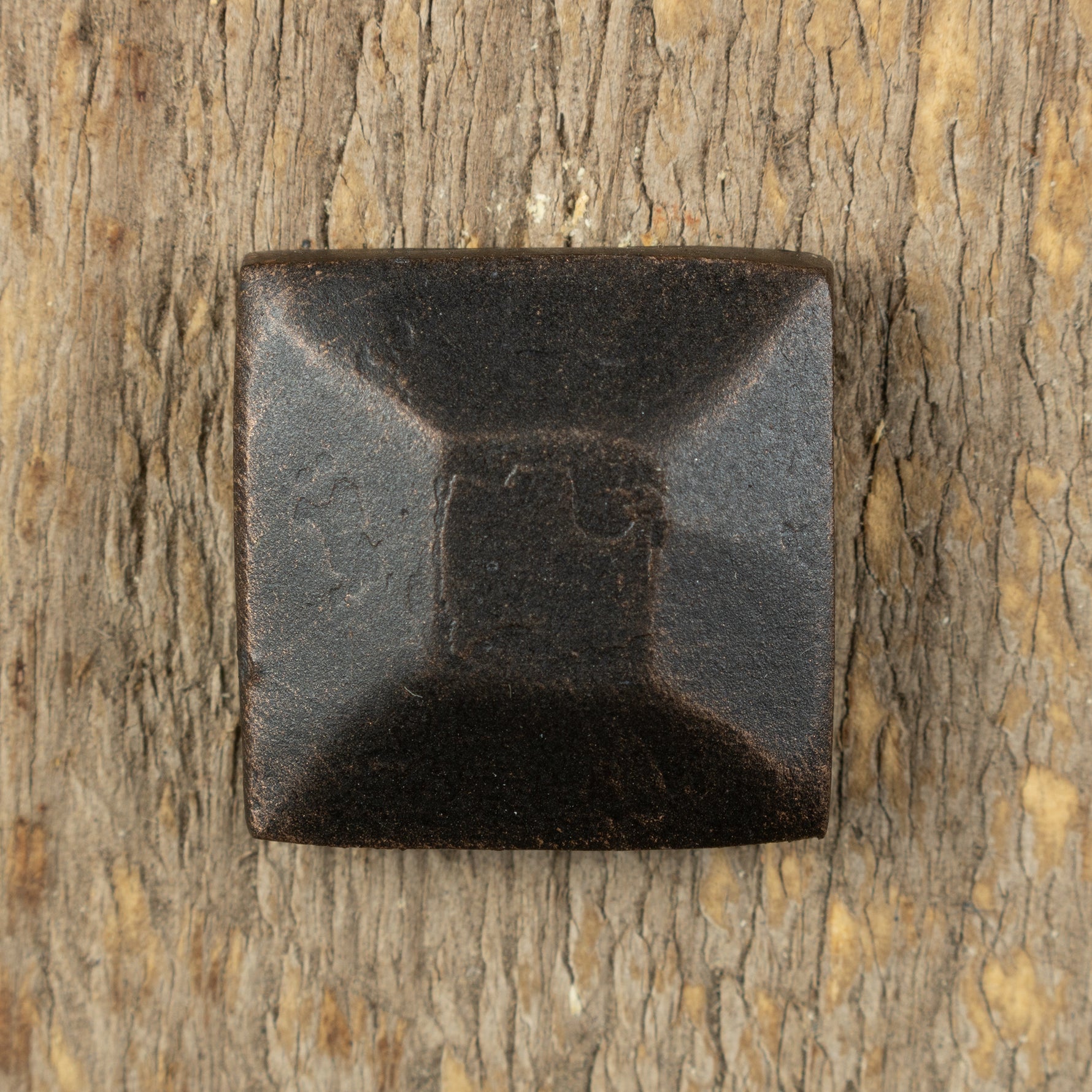 top view of a decorative pyramid hammered square head lag screw in an oil rubbed bronze patina finish against a rustic wood background. 